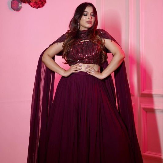 This luxurious wine lehenga set comes with a beautifully hand-embellished cape and crop top, blending modern design with traditional elegance — ideal for destination weddings and special events.