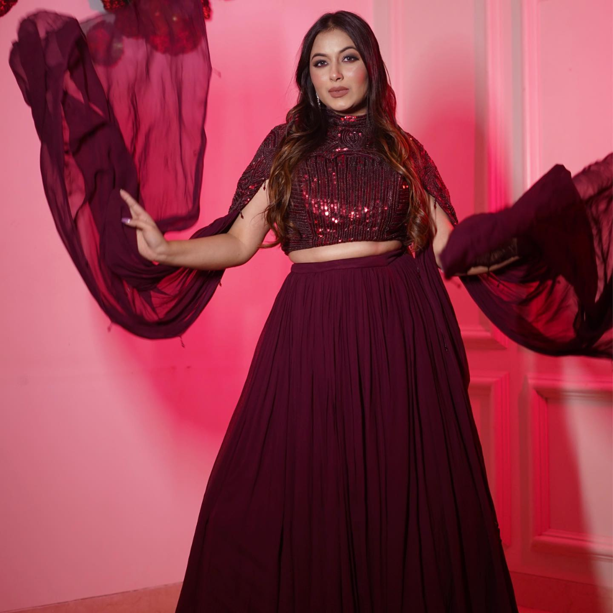 Turn heads in this wine-colored hand-embellished lehenga set featuring a statement cape and crop top. Perfect for brides or bridesmaids at sangeet, cocktails, or receptions.
