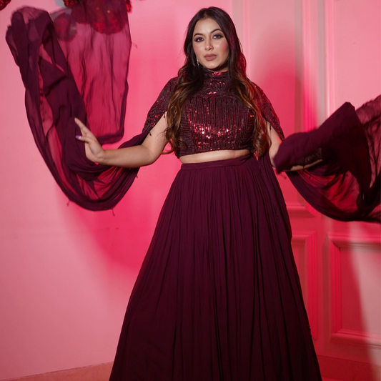 Turn heads in this wine-colored hand-embellished lehenga set featuring a statement cape and crop top. Perfect for brides or bridesmaids at sangeet, cocktails, or receptions.