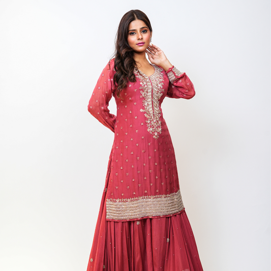 Make a graceful statement in this beautifully hand-embellished rose pink Sharara suit by Nawazish—crafted for celebrations that call for understated elegance and timeless appeal. The kurta features intricate embroidery along the neckline and cuffs, delicately woven in zari, sequin, and threadwork, adding just the right amount of shimmer. The flowy sharara bottoms and subtly adorned dupatta complete this ethereal ensemble, making it a perfect choice for weddings, Eid, pre-wedding and festive gatherings.