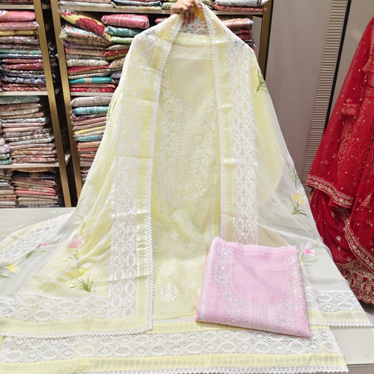 Light yellow embroidered fabric with a pink pocket held up in front of shelves of fabric.